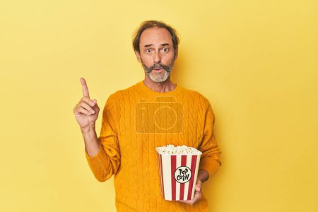 Téléchargez les photos : Homme appréciant pop-corn en studio jaune ayant une bonne idée, concept de créativité. - en image libre de droit