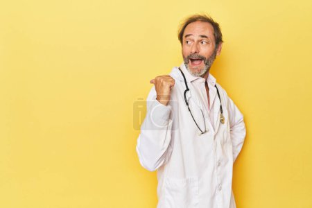 Téléchargez les photos : Médecin avec stéthoscope dans les points jaunes studio avec pouce loin, riant et insouciant. - en image libre de droit