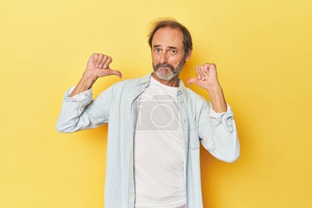 Téléchargez les photos : Homme d'âge moyen caucasien en studio jaune se sent fier et confiant, exemple à suivre. - en image libre de droit