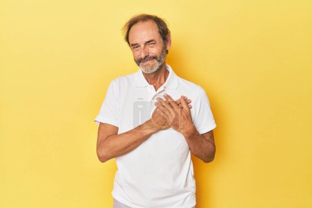 Téléchargez les photos : Homme d'âge moyen caucasien en studio jaune a expression amicale, pressant la paume à la poitrine. Concept d'amour. - en image libre de droit
