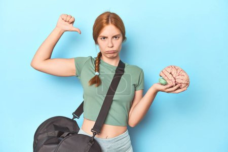 Photo for Sporty redhead with brain model on blue background feels proud and self confident, example to follow. - Royalty Free Image