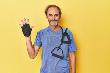 Téléchargez les photos : Homme faisant de l'exercice avec des groupes en studio souriant gai montrant numéro cinq avec les doigts. - en image libre de droit