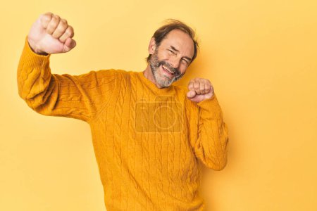 Téléchargez les photos : Homme d'âge moyen caucasien en studio jaune célébrant une journée spéciale, saute et lève les bras avec énergie. - en image libre de droit