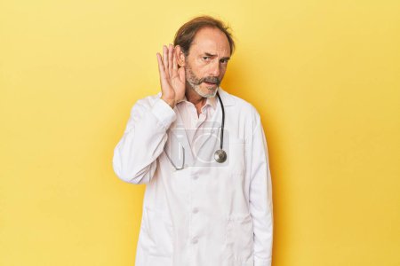 Photo for Doctor with stethoscope in yellow studio trying to listening a gossip. - Royalty Free Image