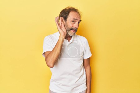 Photo for Caucasian middle-aged man in yellow studio trying to listening a gossip. - Royalty Free Image