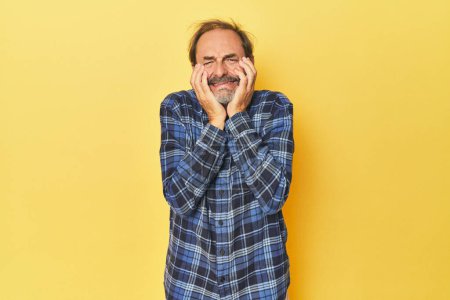 Photo for Caucasian middle-aged man in yellow studio crying, unhappy with something, agony and confusion concept. - Royalty Free Image