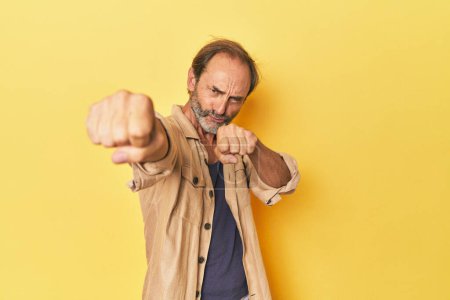 Téléchargez les photos : Homme d'âge moyen caucasien en studio jaune jetant un coup de poing, colère, combats en raison d'une dispute, boxe. - en image libre de droit