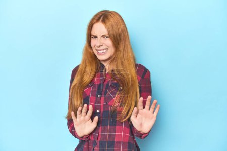 Photo for Redhead young woman on blue background rejecting someone showing a gesture of disgust. - Royalty Free Image