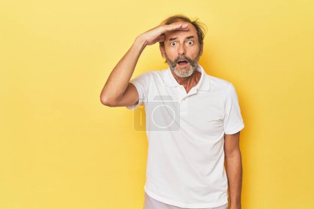 Photo for Caucasian middle-aged man in yellow studio shouts loud, keeps eyes opened and hands tense. - Royalty Free Image