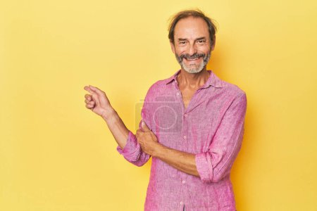 Téléchargez les photos : Caucasien d'âge moyen homme en studio jaune souriant joyeusement pointant avec index loin. - en image libre de droit