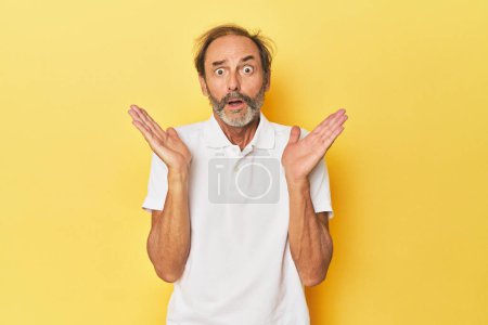 Foto de Caucásico hombre de mediana edad en estudio amarillo sorprendido y sorprendido. - Imagen libre de derechos