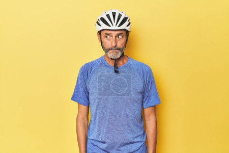 Photo for Cyclist wearing helmet in yellow studio confused, feels doubtful and unsure. - Royalty Free Image