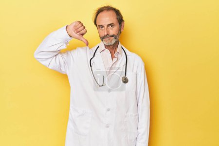 Téléchargez les photos : Docteur avec stéthoscope en studio jaune montrant un geste détestable, pouces baissés. Concept de désaccord. - en image libre de droit