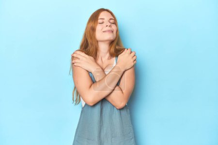 Photo for Redhead young woman on blue background hugs, smiling carefree and happy. - Royalty Free Image