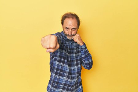 Téléchargez les photos : Homme d'âge moyen caucasien en studio jaune jetant un coup de poing, colère, combats en raison d'une dispute, boxe. - en image libre de droit