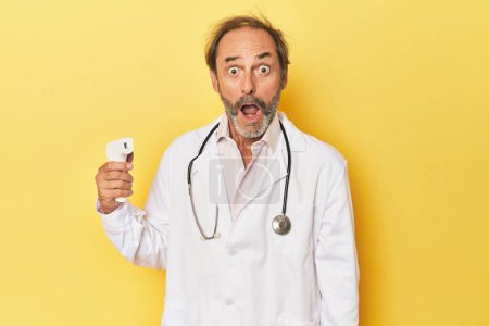 Foto de Doctor sosteniendo termómetro infrarrojo en estudio gritando muy enojado y agresivo. - Imagen libre de derechos