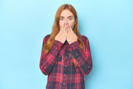 Photo for Redhead young woman on blue background shocked, covering mouth with hands, anxious to discover something new. - Royalty Free Image