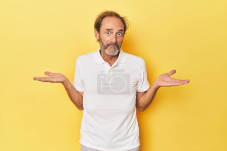 Téléchargez les photos : Caucasien d'âge moyen homme en studio jaune doutant et haussant les épaules en questionnant geste. - en image libre de droit
