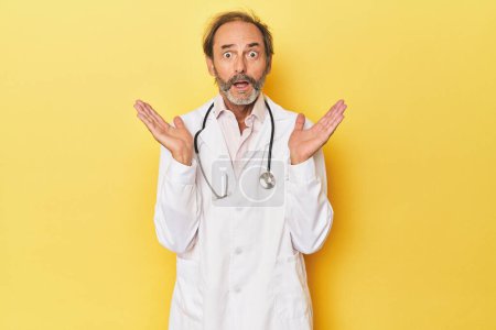 Téléchargez les photos : Médecin avec stéthoscope en studio jaune surpris et choqué. - en image libre de droit