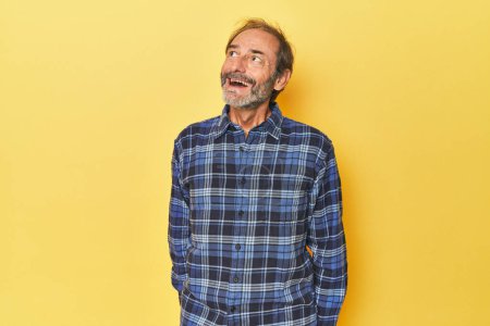 Photo for Caucasian middle-aged man in yellow studio relaxed and happy laughing, neck stretched showing teeth. - Royalty Free Image
