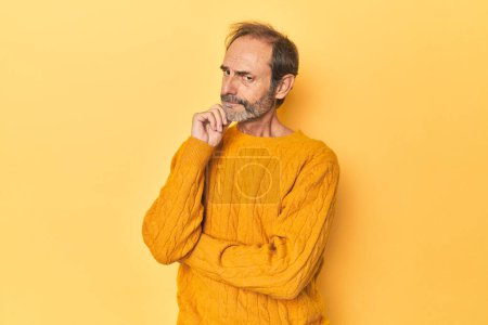 Téléchargez les photos : Homme d'âge moyen caucasien dans un studio jaune penser et regarder vers le haut, être réfléchissant, contempler, avoir un fantasme. - en image libre de droit
