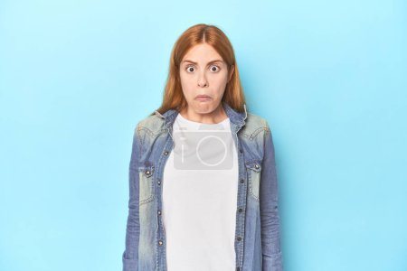 Photo for Redhead young woman on blue background shrugs shoulders and open eyes confused. - Royalty Free Image