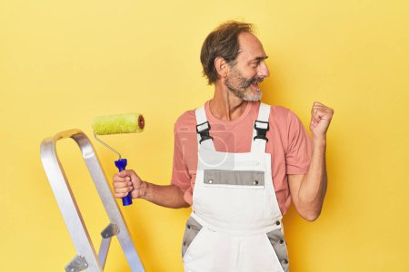 Foto de Hombre pintando fondo amarillo en puntos de estudio con el dedo pulgar lejos, riendo y sin preocupaciones. - Imagen libre de derechos