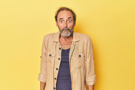 Photo for Caucasian middle-aged man in yellow studio shrugs shoulders and open eyes confused. - Royalty Free Image