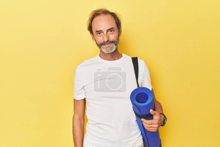 Téléchargez les photos : Homme avec tapis de yoga en studio jaune heureux, souriant et joyeux. - en image libre de droit