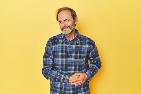 Téléchargez les photos : Homme d'âge moyen caucasien dans un studio jaune ayant une douleur au foie, maux d'estomac. - en image libre de droit