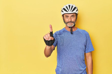 Téléchargez les photos : Cycliste portant un casque en studio jaune montrant numéro un avec doigt. - en image libre de droit