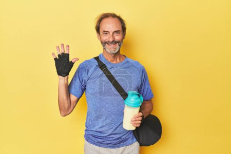 Photo for Gym-goer with protein shake in studio smiling cheerful showing number five with fingers. - Royalty Free Image