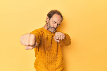 Foto de Caucásico hombre de mediana edad en estudio amarillo lanzando un puñetazo, la ira, la lucha debido a una discusión, el boxeo. - Imagen libre de derechos