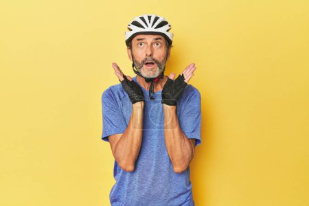 Téléchargez les photos : Cycliste portant un casque en studio jaune surpris et choqué. - en image libre de droit