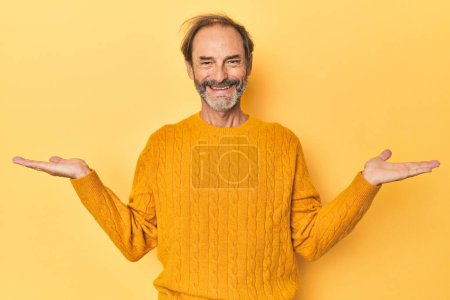 Téléchargez les photos : Blanc homme d'âge moyen en studio jaune fait échelle avec les bras, se sent heureux et confiant. - en image libre de droit