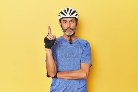 Téléchargez les photos : Cycliste portant un casque en studio jaune ayant une bonne idée, concept de créativité. - en image libre de droit