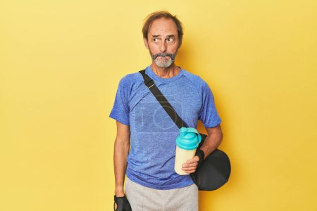 Photo for Gym-goer with protein shake in studio confused, feels doubtful and unsure. - Royalty Free Image