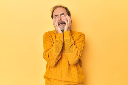 Foto de Caucásico hombre de mediana edad en estudio amarillo lloriqueando y llorando desconsoladamente. - Imagen libre de derechos