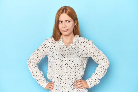 Photo for Redhead young woman on blue background confused, feels doubtful and unsure. - Royalty Free Image