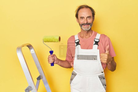 Téléchargez les photos : Homme peignant fond jaune en studio souriant et levant le pouce - en image libre de droit