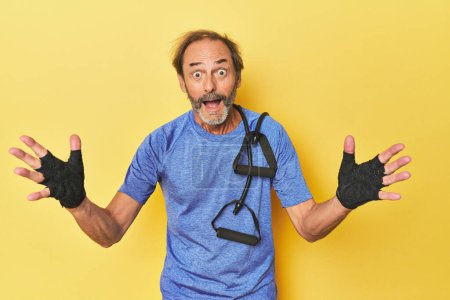Photo for Man exercising with bands in studio receiving a pleasant surprise, excited and raising hands. - Royalty Free Image