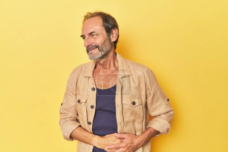 Photo for Caucasian middle-aged man in yellow studio having a liver pain, stomach ache. - Royalty Free Image