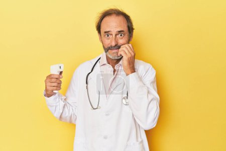 Foto de Doctor sosteniendo termómetro infrarrojo en estudio mordiendo las uñas, nervioso y muy ansioso. - Imagen libre de derechos
