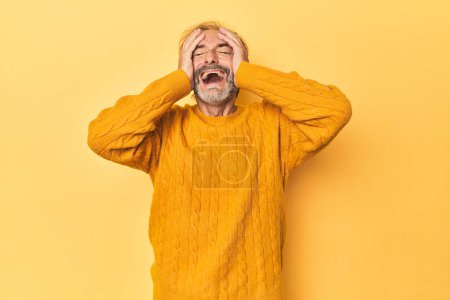 Téléchargez les photos : Homme d'âge moyen caucasien en studio jaune rit joyeusement en gardant les mains sur la tête. Concept de bonheur. - en image libre de droit