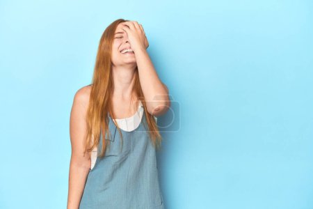 Foto de Pelirroja joven sobre fondo azul riendo feliz, despreocupada, emoción natural. - Imagen libre de derechos