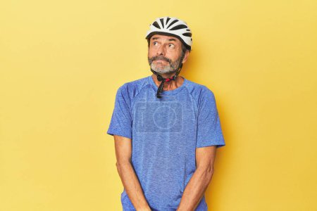 Photo for Cyclist wearing helmet in yellow studio dreaming of achieving goals and purposes - Royalty Free Image