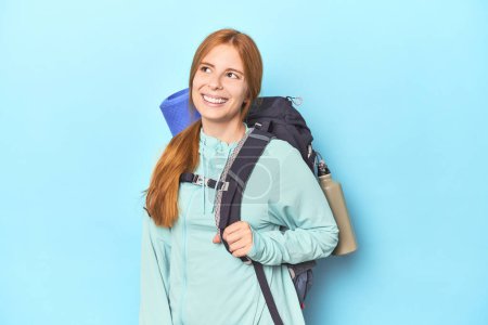 Téléchargez les photos : Voyageur rousse avec sac à dos et tapis en studio rêvant d'atteindre des objectifs et des buts - en image libre de droit