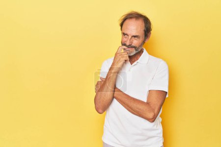 Photo for Caucasian middle-aged man in yellow studio relaxed thinking about something looking at a copy space. - Royalty Free Image