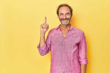 Photo for Caucasian middle-aged man in yellow studio showing number one with finger. - Royalty Free Image