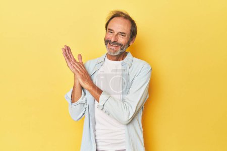 Téléchargez les photos : Homme d'âge moyen caucasien en studio jaune se sentant énergique et confortable, les mains frottées confiantes. - en image libre de droit